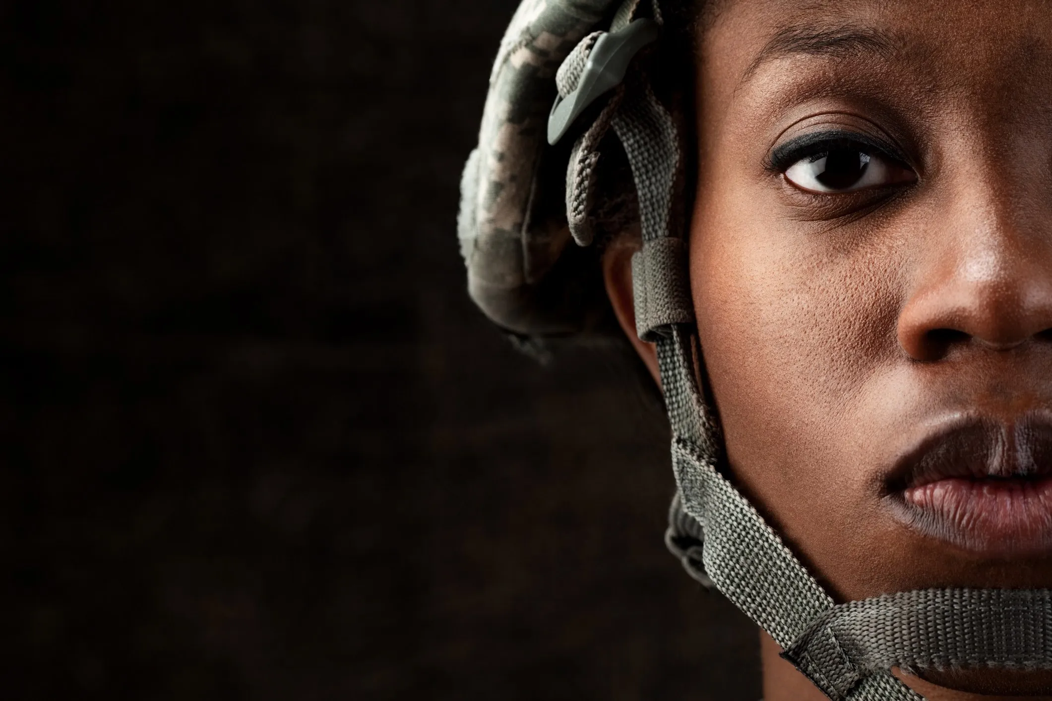 Close up of a woman soldier in a combat helmet, looking straight ahead from the right of the frame, with the Beyond The Uniform logo in the corner
