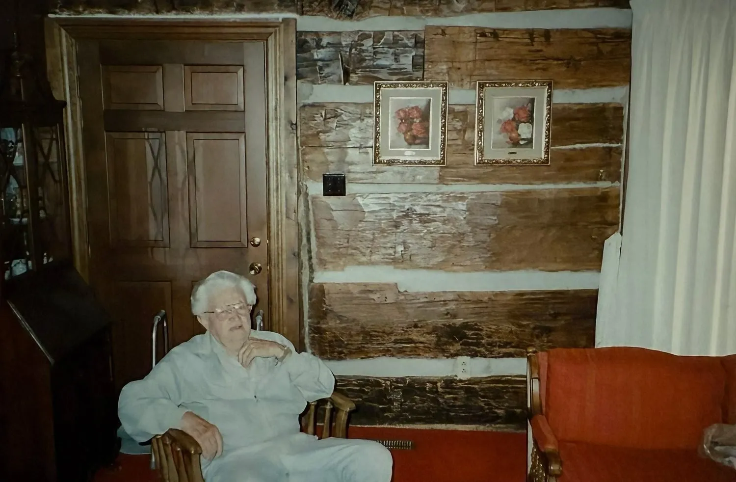 William Brown, the last occupant of the Latimer House, seated inside the log house by the door, the hand hewn logs on the wall behind him