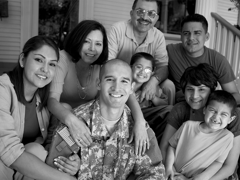 A soldier in camouflage surrounded by his smiling family, in black and white