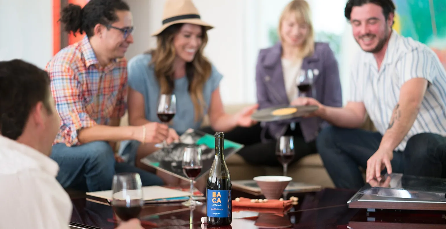 Friends laughing around a coffee table with glasses of red and a bottle of BACA