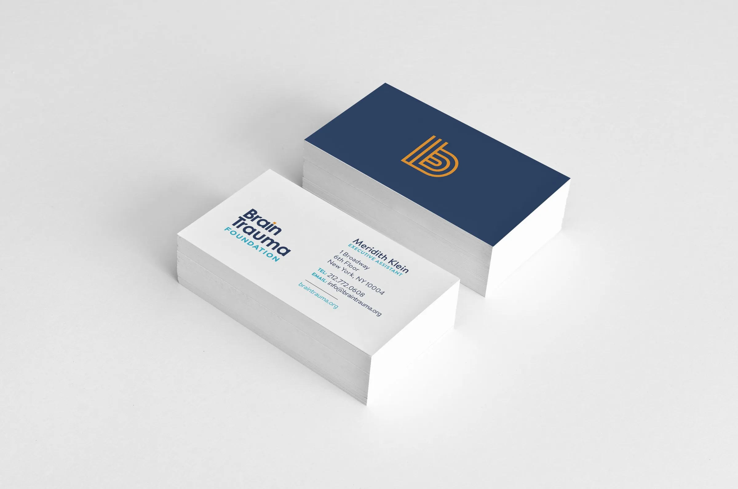 Two stacks of business cards: the white front with the logo and contact details, and the navy back with the orange b