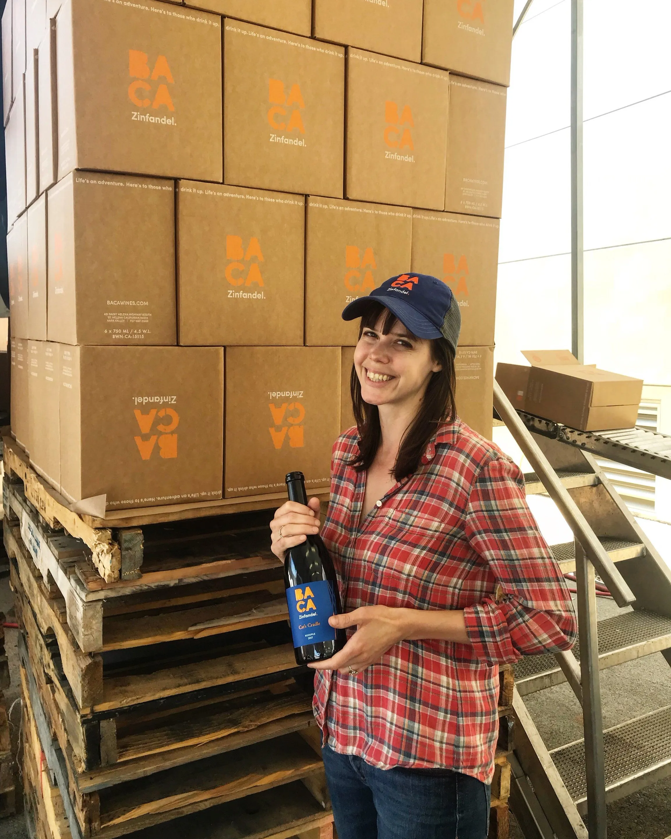 A smiling BACA team member holding a bottle in front of a stack of BACA shippers