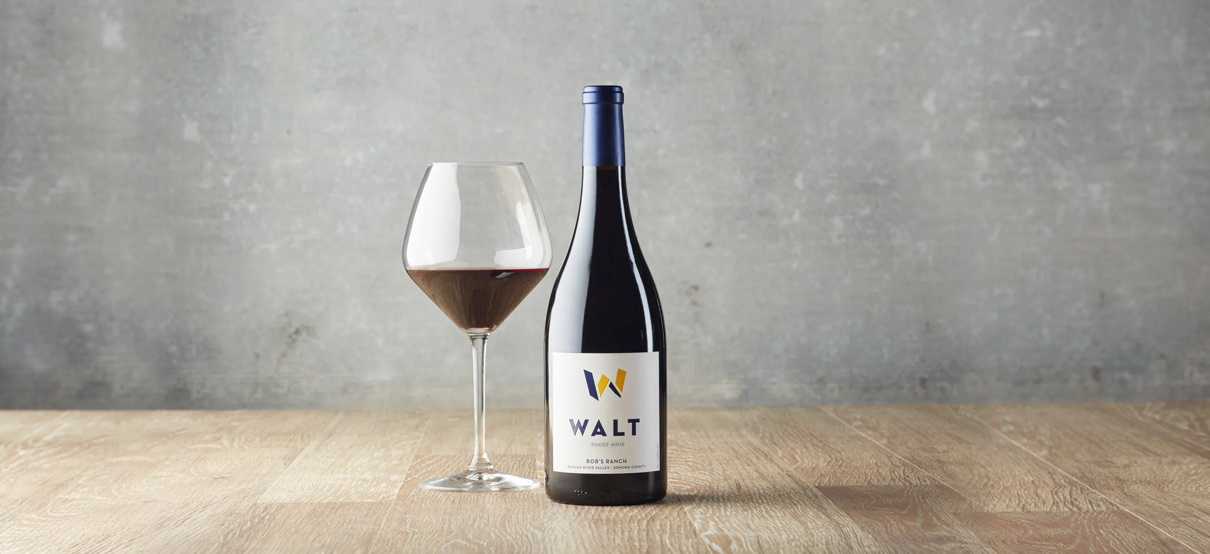 A bottle of WALT Bob’s Ranch Pinot Noir and a filled glass on a wooden table
